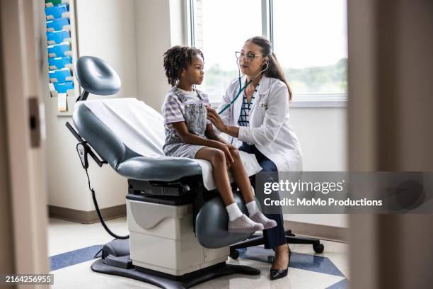 female doctor listening to young girl's heart in exam room - doctor stethoscope patient whole body stock pictures, royalty-free photos & images