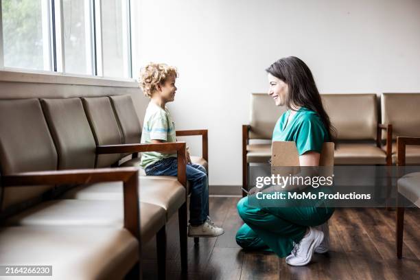 female nurse in scrubs talking with young boy in waiting room - female nurse stock pictures, royalty-free photos & images