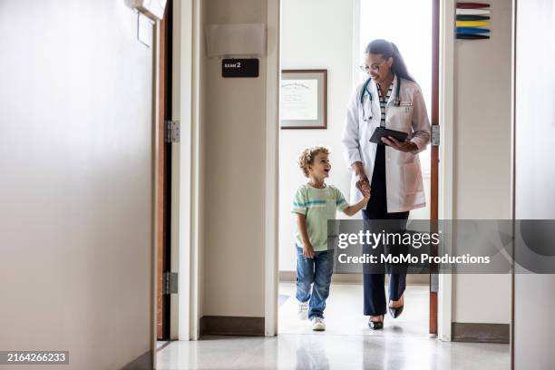 female doctor talking with young boy in doctor's office hallway - doctor stethoscope patient whole body stock pictures, royalty-free photos & images