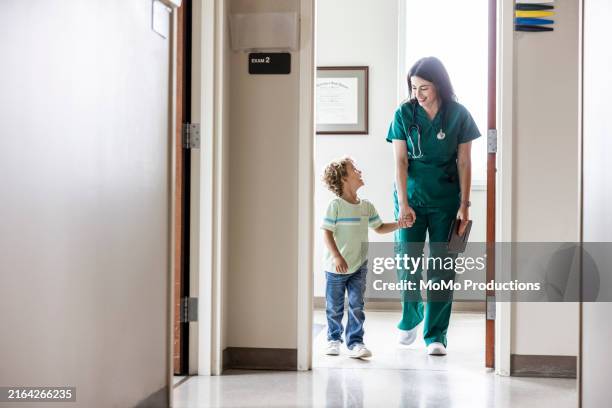 female doctor talking with young boy in doctor's office hallway - pediatric nurse stock pictures, royalty-free photos & images