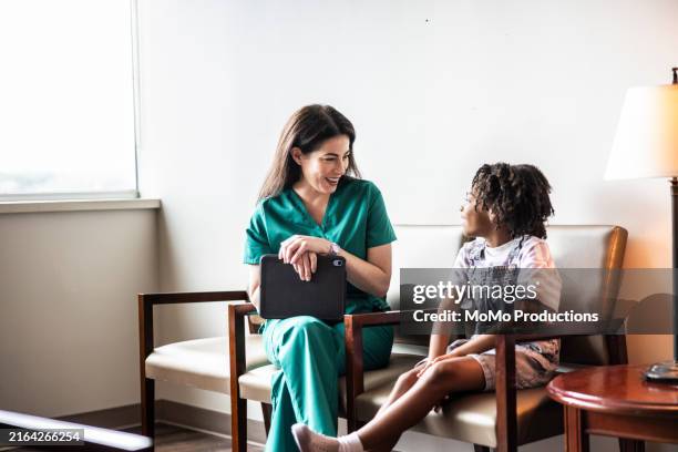 female nurse in scrubs talking with young girl in waiting room - pediatric nurse stock pictures, royalty-free photos & images