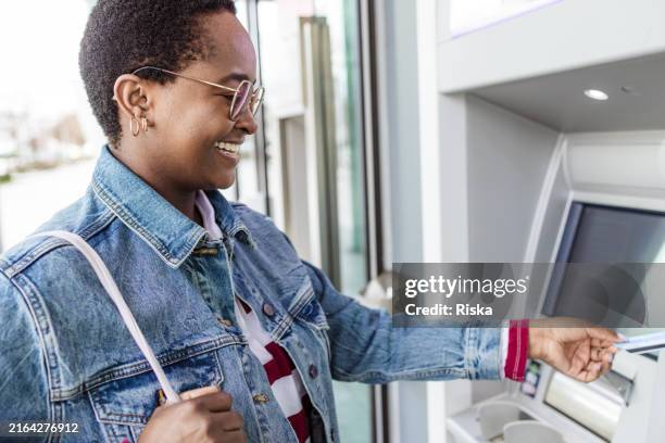 a woman inserting a debit card into an atm - moving toward stock pictures, royalty-free photos & images
