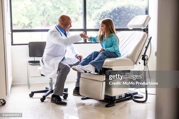 male doctor doing fist bump with young girl in exam room - doctor stethoscope patient whole body stock pictures, royalty-free photos & images