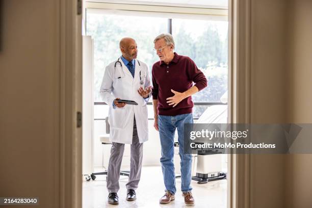 male doctor talking with senior man in exam room - doctor stethoscope patient whole body stock pictures, royalty-free photos & images