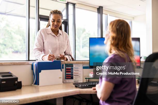 female patient paying with credit card at doctor's office front desk - krankenversicherung stock-fotos und bilder