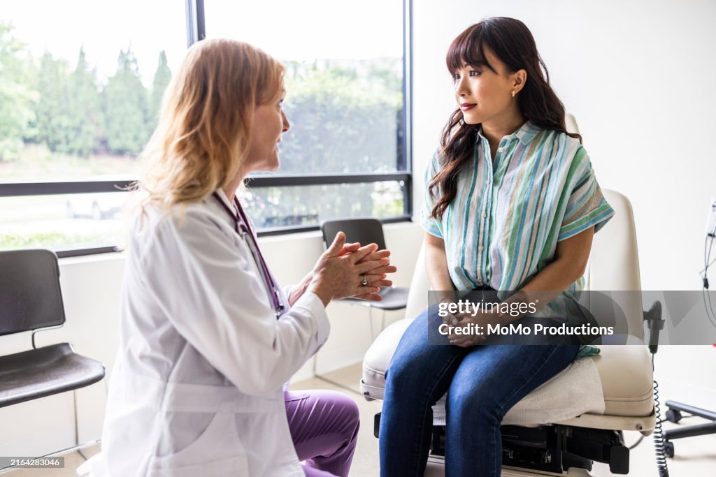 Female doctor talking with young woman in exam room
