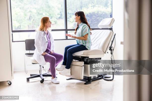 female doctor talking with young woman in exam room - gynäkologe stock-fotos und bilder