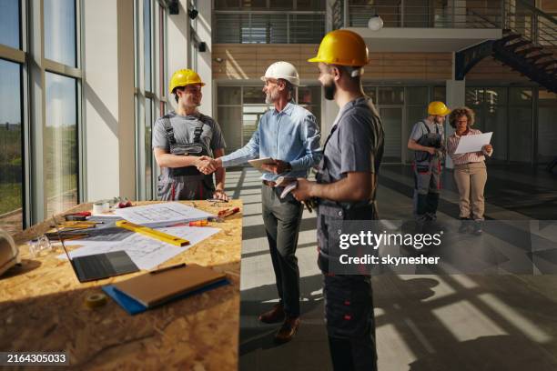 feliz gerente de proyecto saludando a un trabajador de la construcción en el edificio. - estructura de edificio fotografías e imágenes de stock