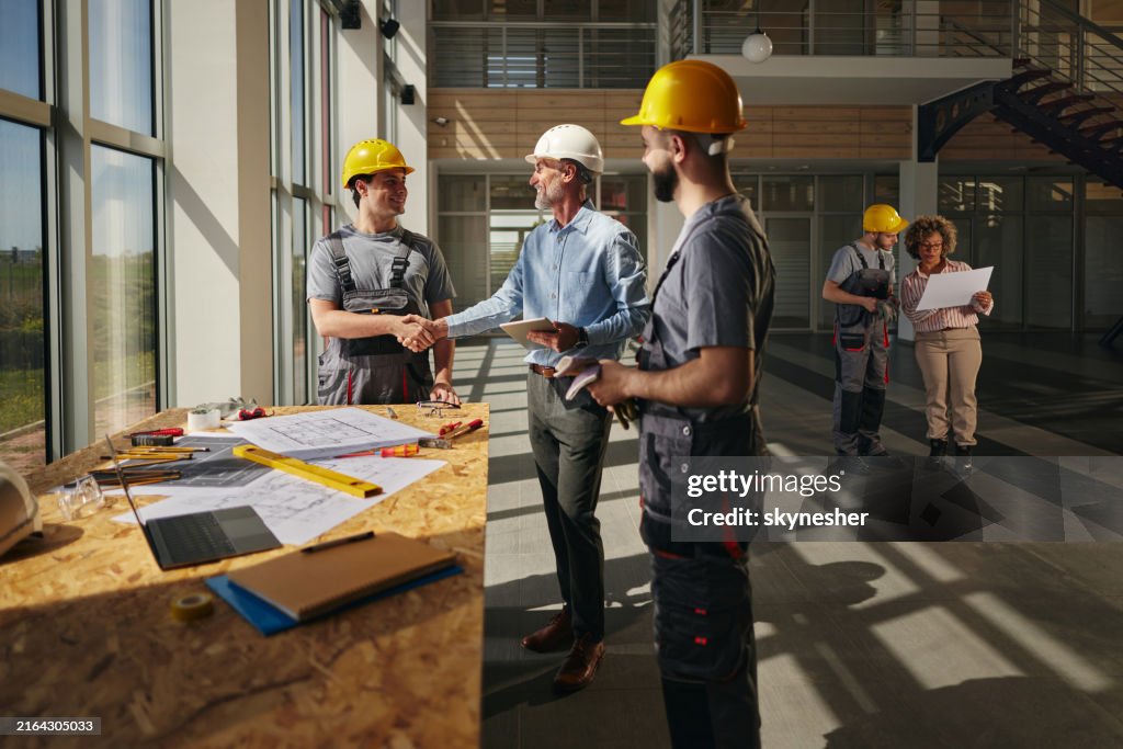 Happy project manager greeting a construction worker in the building.
