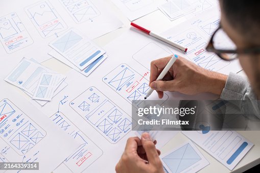 Designer de UX/UI trabalhando em wireframes para um protótipo de site e aplicativo móvel, cercado por esboços de fluxo de usuário e ferramentas de design, em conceito de design de site e aplicativo móvel. Designer de UX/UI trabalhando em wireframes para um protótipo de site e aplicativo móvel, cercado por esboços de fluxo de usuário e ferramentas de design, em conceito de design de site e aplicativo móvel.