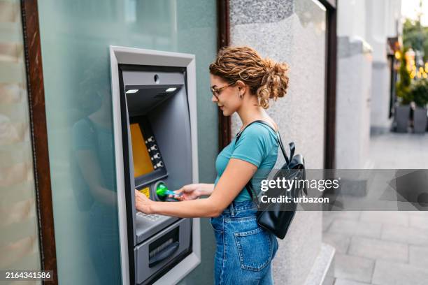 young woman withdrawing money using a credit card at the atm machine in budapest in hungary - atm stock pictures, royalty-free photos & images