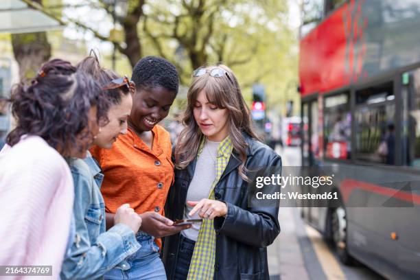 female friends sharing smart phone in city - city break stock pictures, royalty-free photos & images