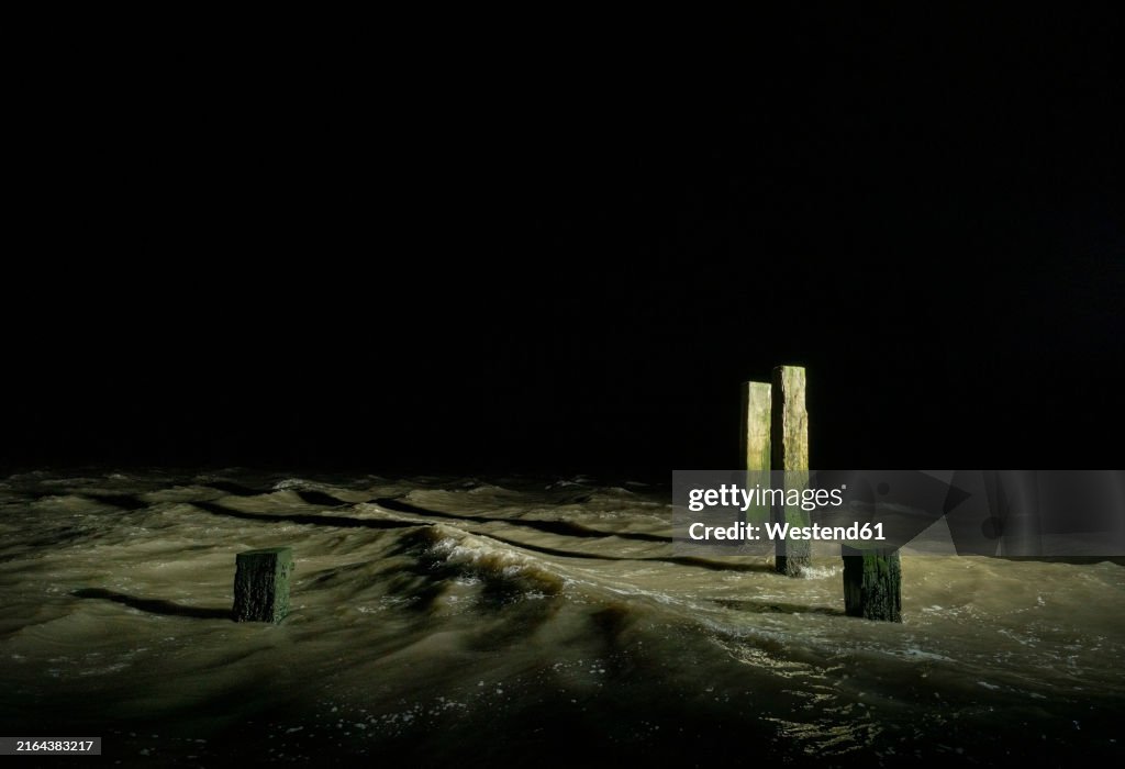 Illuminated wooden posts in Wadden Sea at night