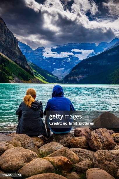 woman and her son sitting at beautiful lake louise in alberta in canada - lake louise stock pictures, royalty-free photos & images