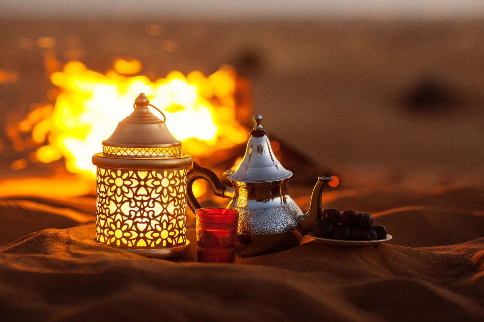 Dates, Teapot, Cup With Tea Near The Fire In The Desert With A Beautiful Background. Ramadan Kareem Dates, Teapot, Cup With Tea Near The Fire In The Desert With A Beautiful Background. Ramadan Kareem