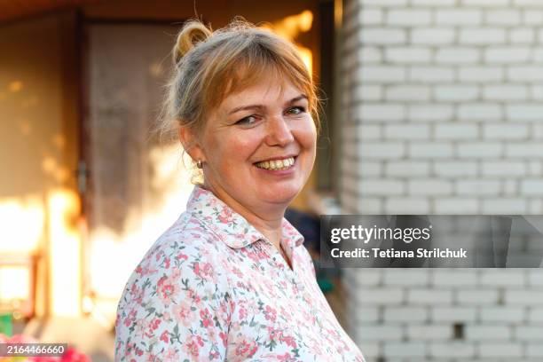 Portrait of a smiling mature woman in a summer. A middle-aged Caucasian blonde woman in her 40s is pictured against a backdrop of break house
