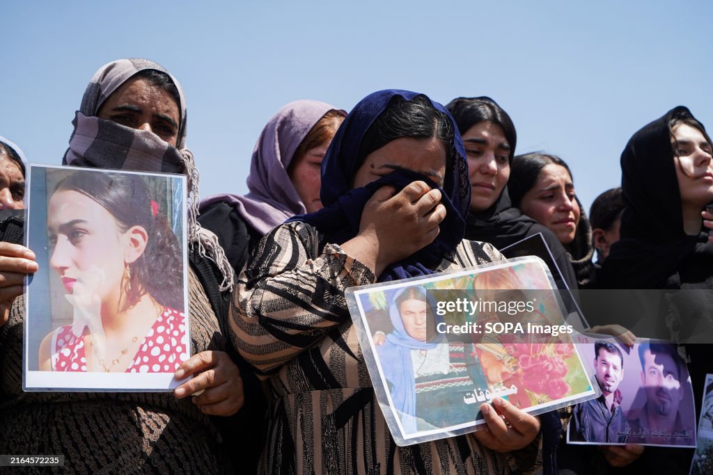 Iraqi Yazidi women cry as they hold pictures of their...