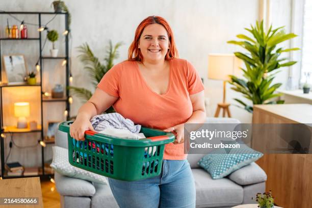 junge frau, die einen wäschekorb im zu hause im wohnzimmer trägt - trockner stock-fotos und bilder