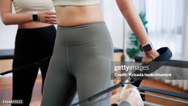 young asian woman learning to do a pilates move with resistance bands on a reformer. - virilha humana imagens e fotografias de stock