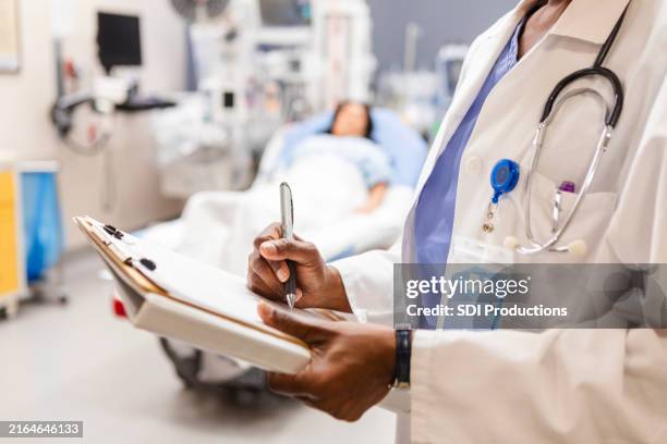 ein nicht wiederzuerkennender arzt schreibt notizen in die krankenakte des patienten - intensivstation stock-fotos und bilder