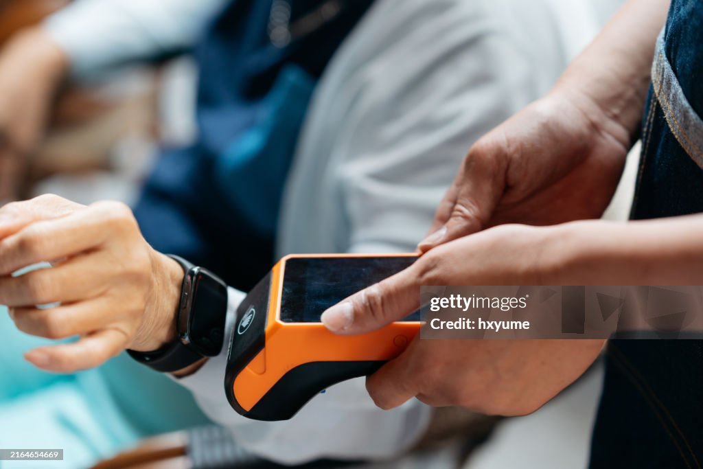 Close up shot of a senior adult paying with smartwatch at restaurant. Contactless and mobile payment concept.