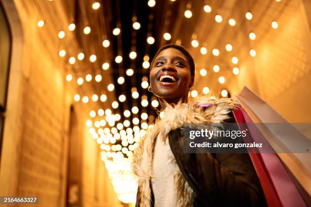 young african american woman joyfully shopping at night with festive christmas lights - woman shopping stock pictures, royalty-free photos & images