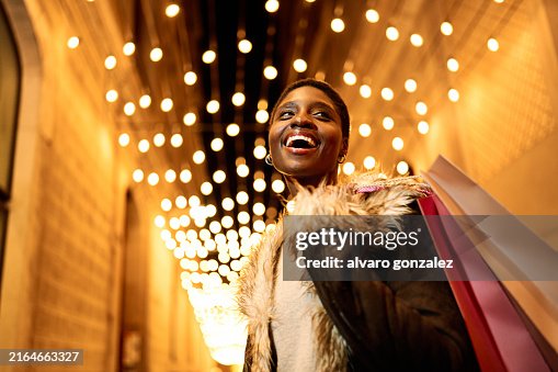 Young African American woman joyfully shopping at night with festive Christmas lights Young African American woman joyfully shopping at night with festive Christmas lights