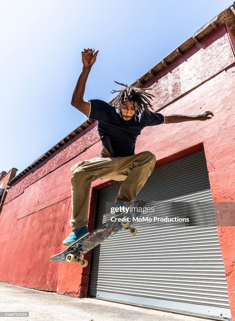 Skateboarder performing trick in front of red industrial building