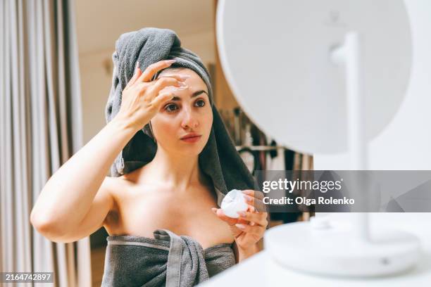 serum application for hyperpigmentation. woman in towel applies moisturizing serum on face for youth. - hyperpigmentation stockfoto's en -beelden
