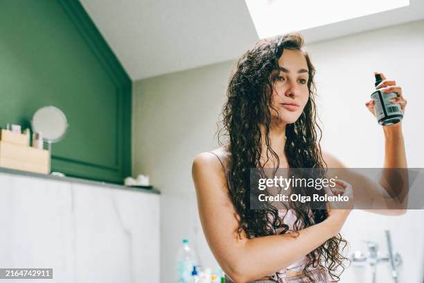 curly hair care: woman uses oil for curly method to restore hair length at home - hair conditioner stock pictures, royalty-free photos & images