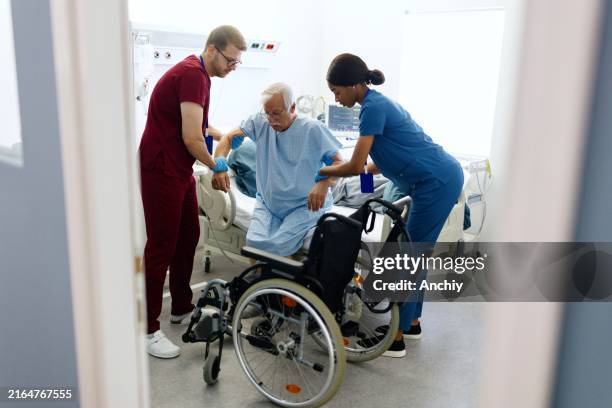 medical workers helping patient to get into a wheelchair - physical activity stock pictures, royalty-free photos & images