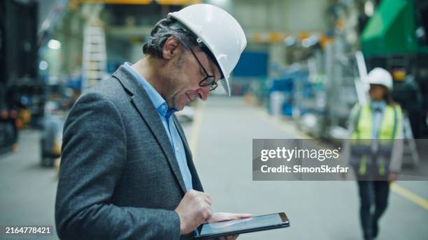 male inspector works on tablet pc in factory. scene shows use of technology in monitoring and improving factory processes and conditions - scrutiny stock pictures, royalty-free photos & images