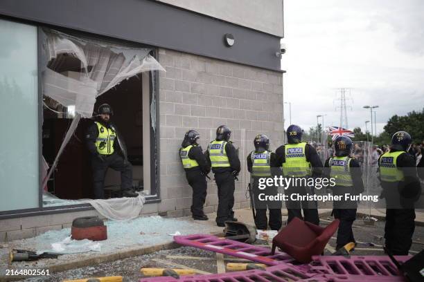 Riot police create a barricade in front of windows broken during riots between anti-migration protesters outside of the Holiday Inn Express in...