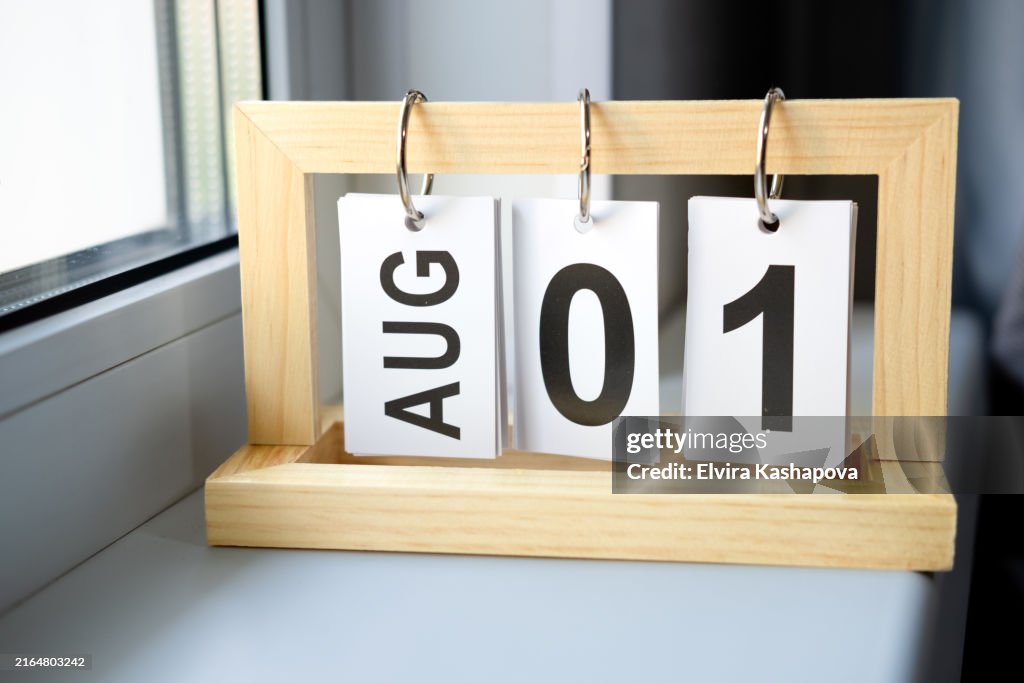 Wooden desk calendar with the date August 1 on the windowsill against the background of the window