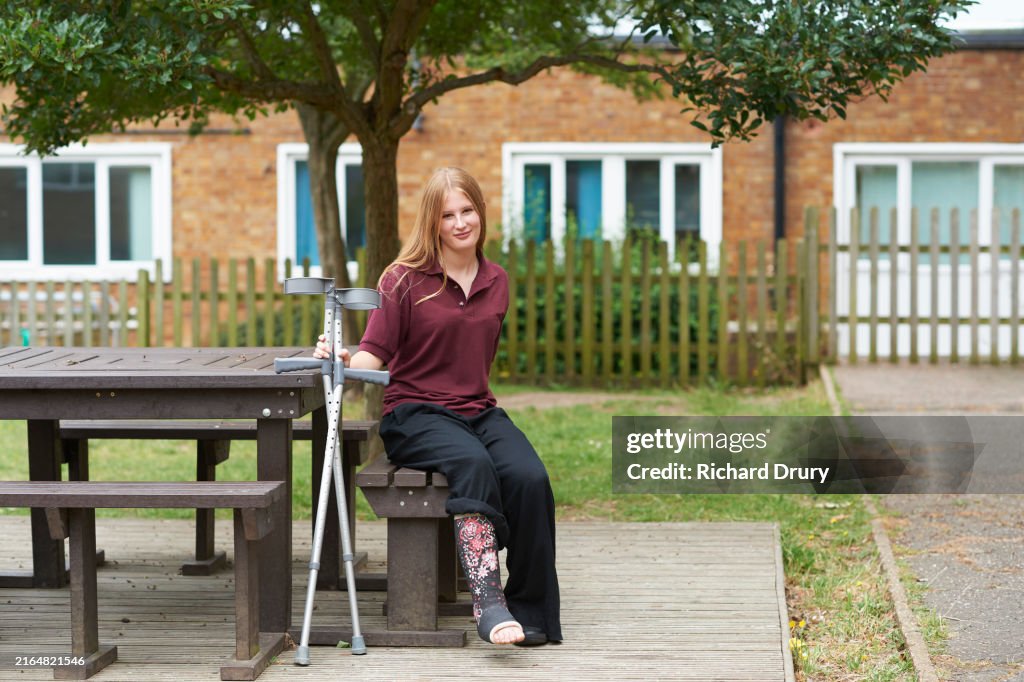 A portrait of a high school student with crutches sitting outside her school