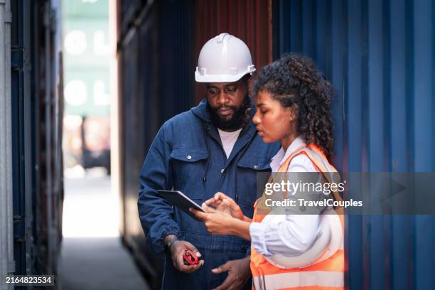 confident engineer and tablet at containers yard from cargo freight ship for import export. dock control worker wearing protective coveralls against stack of a containers terminal. colleagues talk about logistics operations. import and export concept - ship engineer stock pictures, royalty-free photos & images