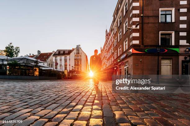 rear view of a man exploring cobblestone streets of riga old town at sunrise, latvia - riga latvia stock pictures, royalty-free photos & images