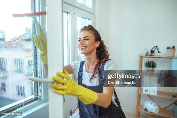 bella giovane donna sorridente che pulisce la finestra con il lavavetri - impresa di pulizie foto e immagini stock