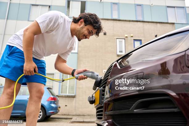 the young man is charging his electric car. - elektrische auto stockfoto's en -beelden