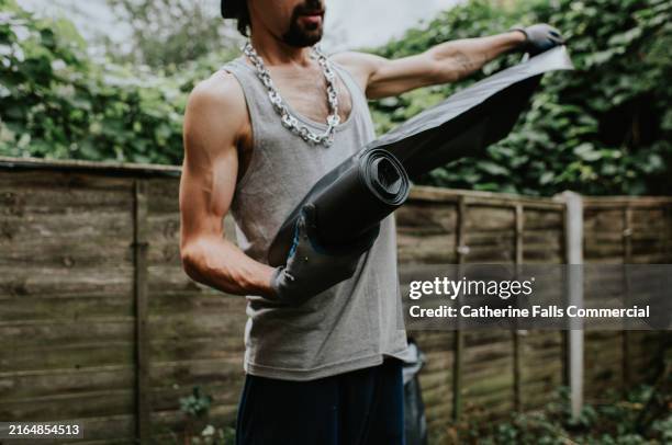 a man separates some large, black, bin bags with serrated lines in a small back yard - müllmann stock-fotos und bilder