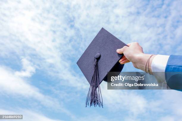 hand holding graduation hat against a blue sky - birrete fotografías e imágenes de stock