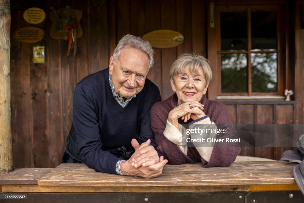 Smiling senior couple leaning on railing of a rural wooden house