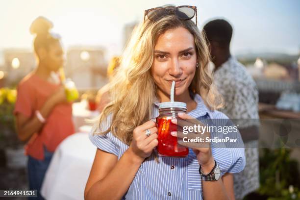 junge kaukasische frau, die mocktail trinkt, während einer party auf dem dach mit ihren multiethnischen freunden - alkoholfrei stock-fotos und bilder