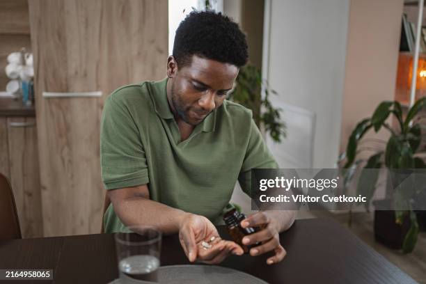 young black man at home taking his daily medicine with a glass of water - dark skin tone stock pictures, royalty-free photos & images