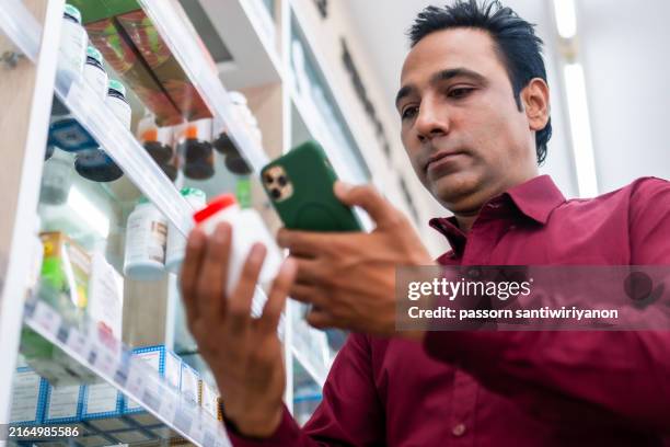 a customer in a pharmacy store examines a medicine bottle while using a smartphone, highlighting modern healthcare and retail services. - chemist sign stock pictures, royalty-free photos & images