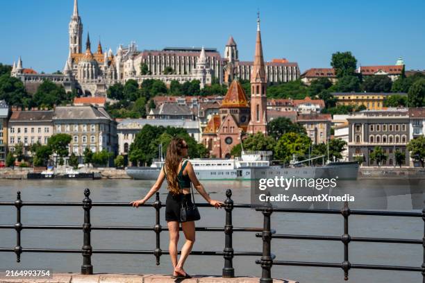 woman looks across river to city skyline - riverbank stock pictures, royalty-free photos & images