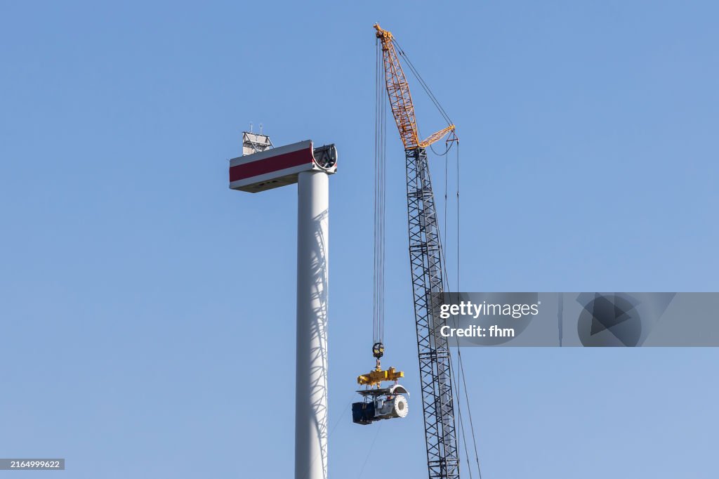 Wind turbine construction site - large crane lifts turbine on the tower