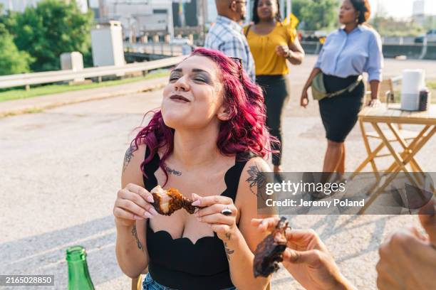 Cheerful young woman enjoying a Barbecued Chicken Drumstick outdoors at a BBQ Food Truck in Houston, Texas