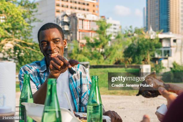 Young Black Man Pointing And Joking While Pointing With A Chicken Wing While Eating With Friends Outdoors At A Bbq Food Truck In Houston Texas High-Res Stock Photo