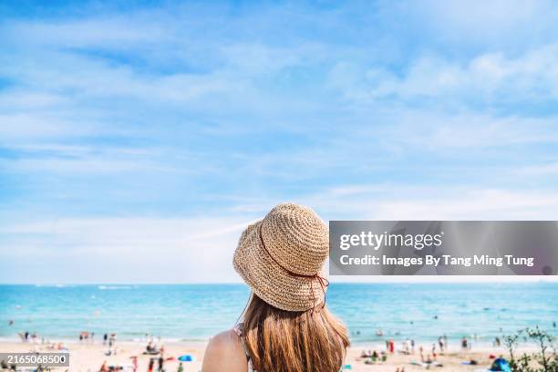 rear view of a young woman in straw hat looking out to the sea at beach in a sunny day - horizon stock pictures, royalty-free photos & images